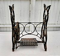 Front side of antique cast metal sewing machine frame with treadle pedal and handwheel visible.