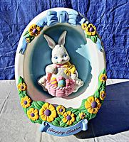Front view showing the detailed bunny holding a basket with colorful Easter eggs, surrounded by yellow flowers and a 'Happy Easter' banner at the bottom.
