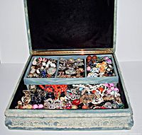 Open view of the jewelry box showing dark blue velvet interior lining and a removable tray filled with assorted colorful vintage costume jewelry including clip earrings, necklaces, rings, and pins.