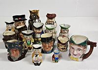 Photo of 16 miniature Toby mugs arranged closely together, showing various facial expressions and hat types, highlighting the detailed character design and different colors including a metallic one.