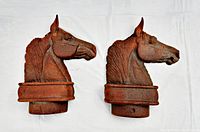 Pair of rusty cast iron horseheads positioned side by side showing left side profiles on white background.