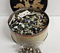 Front view of the tin with assorted buttons, tin open showing button contents, plastic bag of metal buttons placed in front.