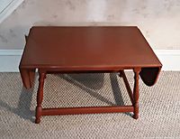 Photo showing the coffee table with the hinged end panels folded down, displaying the compact size and turned wood legs.