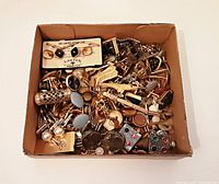 Overhead view of cardboard box filled with various men's cuff links, tie clips, and a few money clips.