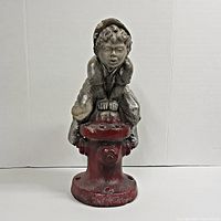 Front view of the concrete statue showing the boy perched on the red fire hydrant with detailed facial features and baseball outfit.