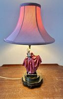 Front view of the lamp illuminated, showing pink fabric shade and porcelain lady figure in pink dress.