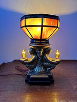 Front view of illuminated lamp showing amber glow of shade and two cherub arm bulbs