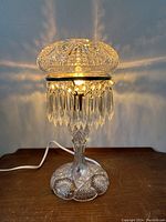 Front view of lamp illuminated showing crystal shade, hanging prisms and base