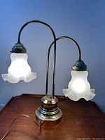 Front view of twin-shade table lamp with lit frosted glass shades and polished brass arms and base.