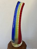Side view of tall bent neck Murano glass vase showing vertical rainbow stripes and control bubble texture.