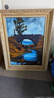 Frontal view of oil painting on canvas with carved frame showing a stone arch bridge with tree and stream below, signed Neogrady.