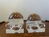 Pair of clear lucite spherical paperweights resting on matching square bases, each with a concave seat for the sphere.