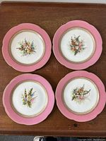 Four Royal Worcester pink band cabinet plates with different hand-painted floral bouquet designs, arranged on a wood surface, showing overall condition and design variety.