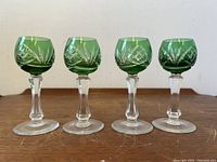 Group of four antique Bohemian cordial glasses with emerald green etched bowls and clear stems on wood surface.