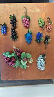 Top view showing all 13 art glass grape bunches arranged on table, showing variety of colors and sizes from about 3 to 8 inches in length.