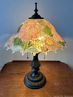 Front view of the tactile pink floral art glass shaded table lamp on a wooden surface.