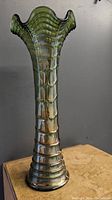 Full view of tall greenish iridescent carnival glass vase with ripple pattern and ruffled top.
