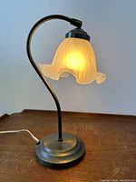 Side view of vintage desk lamp illuminated showing curved arm and floriform glass shade casting warm light