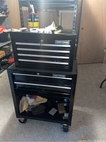 Front view of black Craftsman rolling tool cabinet with top chest, showing Craftsman logo, key lock, wheels, and contents inside lower cabinet.