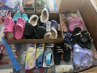 Full view of various Crocs clogs and several pairs of flip flops with Dr. Scholl's insoles laid in front