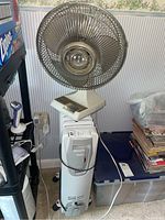 White vintage Windmere 12-inch oscillating fan mounted on top of DeLonghi space heater with visible controls and cage.