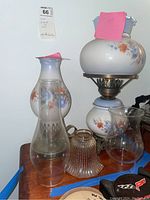 Overall view of lamps and globes with floral painted designs on glass shades and additional clear glass lamp globes