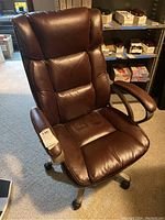 Brown leather office chair angled view showing padded armrests, cushioned seat and backrest, on caster wheels.