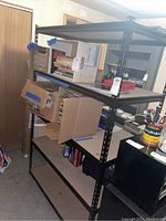 Full view of the shelving unit showing four wood-patterned shelves and black metal frame with items on the shelves that are not included in the lot.