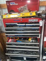 Full view of the red tool chest with seven drawers open showing various hand tools and a yellow Stanley ProBeam level on top