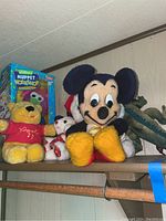 Wide shot of multiple vintage plush toys including Mickey Mouse, Winnie the Pooh, small teddy, green dinosaur, and boxed Jim Henson Muppet Workshop toy.
