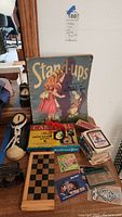Full view of the lot showing the vintage Alice in Wonderland Stand-Ups display, Carnival The Show Business game box, playing cards, chess board, boot toy, and cards.