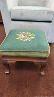 Green cushioned vintage footstool with embroidered floral pattern on wooden cabriole legs.