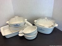 Full view of all Corningware pieces showing the blue cornflower motif including lidded casserole dishes, one covered pan, and nested small handled bowls.