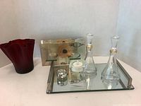 Full lot view showing red glass wavy vase, mirrored tray with glass decanters, small jar, candle holder, and photo frame