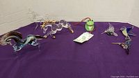 Lot of glass animal figurines and frog toy displayed on purple background