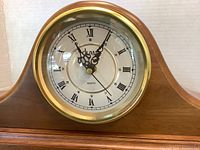 Close-up of Dumai clock face showing Roman numerals, ornate black hands, and the Dumai brand name, set in a gold-tone bezel.