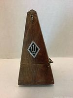 Front view of the vintage wooden pyramid-shaped metronome showing the wood texture and front emblem.