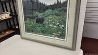 Full view of framed numbered print by RS Parker depicting a bear in nature with forest background and flowers.