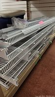 Stacked white metal wire grid shelving racks, showing size and condition