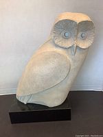 Front view of the light-colored stone owl sculpture with detailed eyes and perched on a black rectangular base.