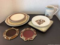 Group of vintage plates, two Hummel plates, white ceramic pitcher, and two ornate picture frames.