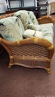 Front left three-quarter view of rattan sofa with cushions and throw pillow