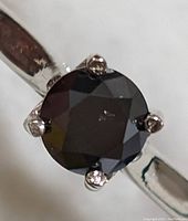 Top view of round black diamond center stone in six-prong setting on white gold band