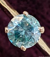 Close-up of round-cut blue moissanite stone in four-prong 10K gold setting.