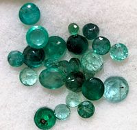 Loose genuine emerald gemstones of various sizes and cuts on a white background.