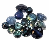 Loose faceted gemstones in shades of blue and green, including oval and round cuts.