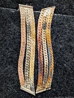 Pair of long, narrow earrings with wavy intertwined strips in silver, gold, and copper tones on black background
