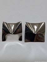 Front-facing photo of the pair of silver square-shaped geometric earrings showing their reflective polished surfaces and concave design.