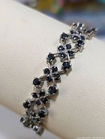 Close-up angled view of the sterling silver bracelet showing the deep blue round saphires arranged in linked X-shaped clusters.