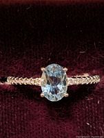 Front close-up view of sterling silver ring with oval blue topaz stone and CZ accents on band.